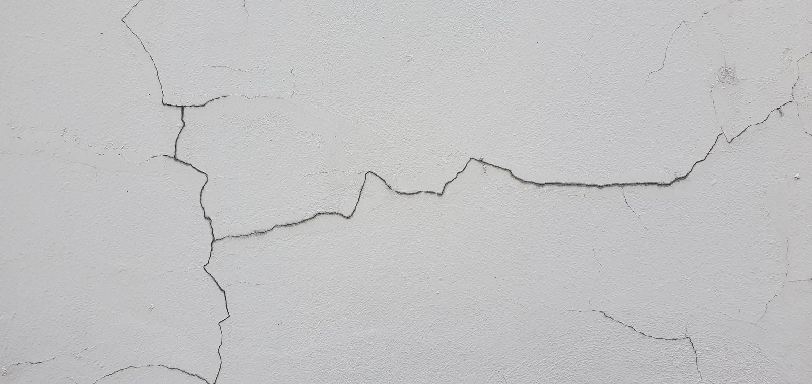 Long horizontal fissure across a white painted cement wall